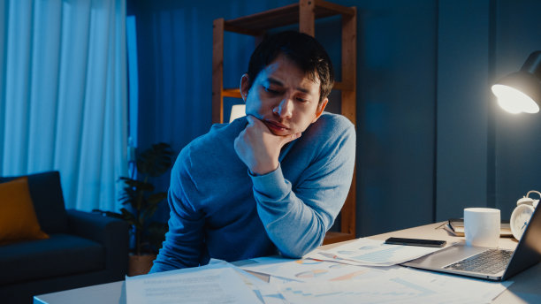 亚洲自由职业者专注于笔记本电脑的工作类型，忙着在家里客厅的桌子上放满文书工作图表，晚上加班。图片下载