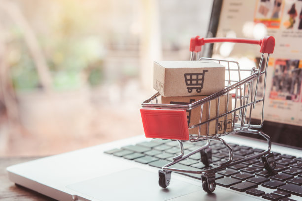 在线购物。在笔记本电脑键盘上的手推车上有一个带有购物车标志的纸板箱。网上购物服务。提供送货上门图片下载