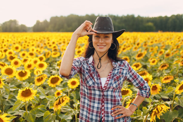 年轻女子农学家戴着牛仔帽，格子衬衫和牛仔裤在向日葵田。丰收的概念。图片下载