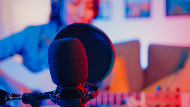 快乐亚洲女孩博主弹吉他，用麦克风唱歌曲录音音乐混音在笔记本电脑在现代客厅家庭工作室晚上。图片下载