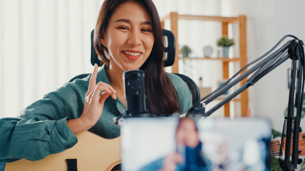 十几岁的亚洲女孩影响者用智能手机播放吉他音乐，用麦克风录音供在线观众在家收听。图片下载