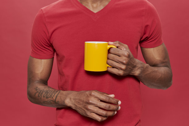 一名身穿红色t恤、手拿黄色马克杯、背景为红色的黑人图片下载