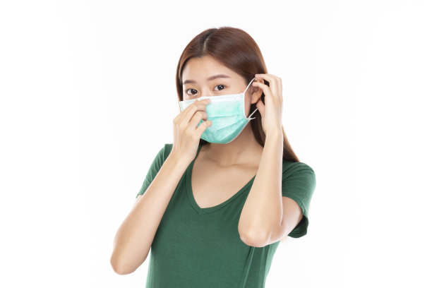 白人背景的年轻亚洲少女。亚洲妇女佩戴医用口罩，预防冠状病毒(Covid-19)。休闲亚洲女人穿绿色t恤在白色的背景。图片下载