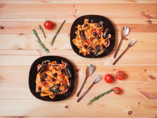 木桌上放着海鲜意面和番茄酱，旁边放着樱桃番茄和迷迭香。前视图。图片下载