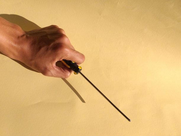 黄色背景下一只手拿着螺丝刀的照片图片下载