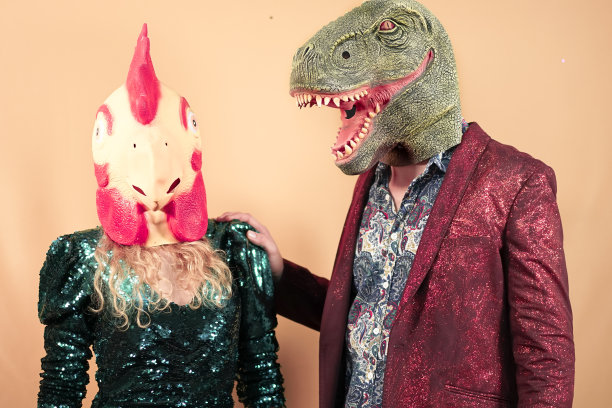戴着霸王龙、恐龙和小鸡面具的夫妇。疯狂的朋友在庆祝派对。荒诞和超现实的滑稽概念。黄色背景。图片下载