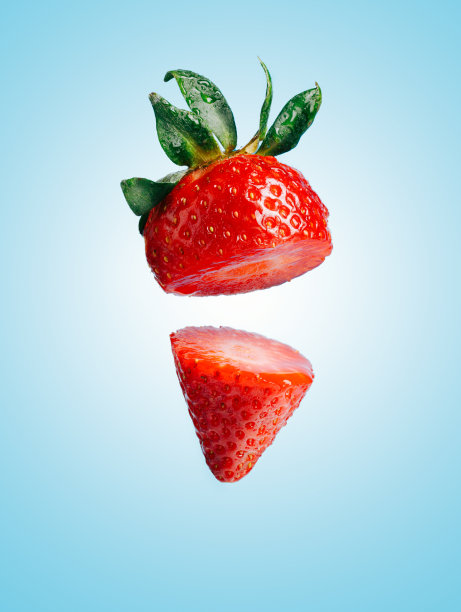 将草莓切成两半，在柔和的蓝色背景下飞舞的夏日水果。创新食品的概念。健康素食饮食标语。图片下载