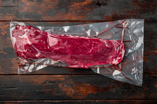 里脊牛肉真空袋真空,黑暗在旧木桌上背景,顶视图平图片下载