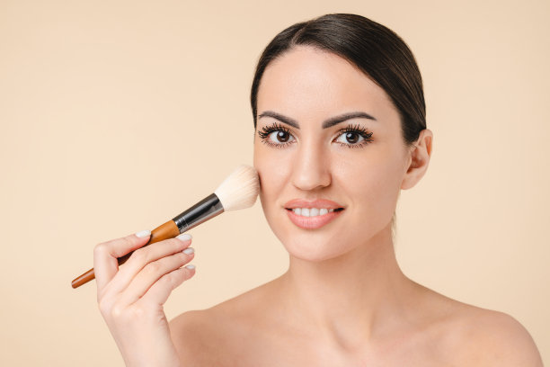 迷人的年轻白人女性在裸露的肩膀上用腮红刷化妆，美容概念图片下载