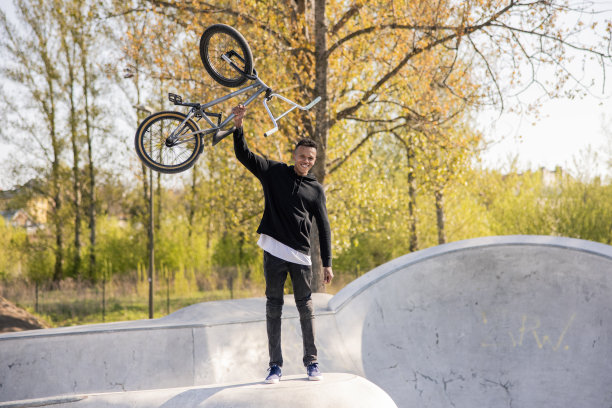 一个有趣的小男孩站在公园的坡道上，脸上带着满意的表情，把他的自行车举过头顶，表示胜利，他很高兴，他赢得了自行车比赛图片下载