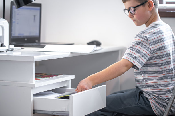 一个小学生坐在桌子旁，从抽屉里拿出一些东西。图片下载