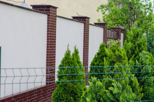 绿色的树在一个白色和红色的石头篱笆的背景。景观。图片下载