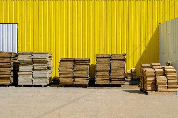 一堆堆光滑的工业用木托盘靠着一堵黄色的墙。图片下载