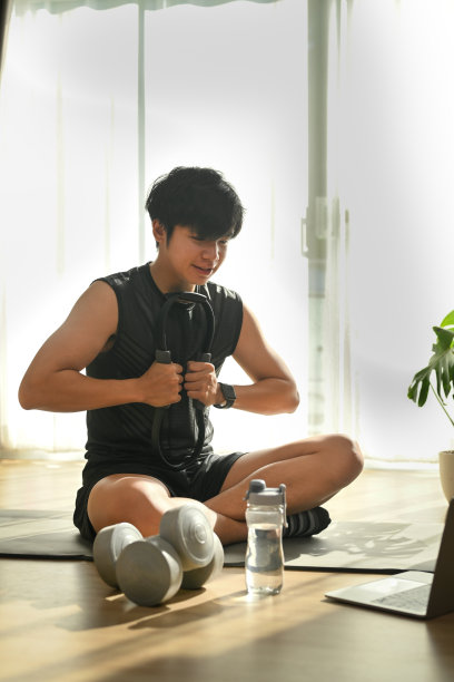 一个快乐的年轻人坐在瑜伽垫上，在客厅里锻炼。图片下载