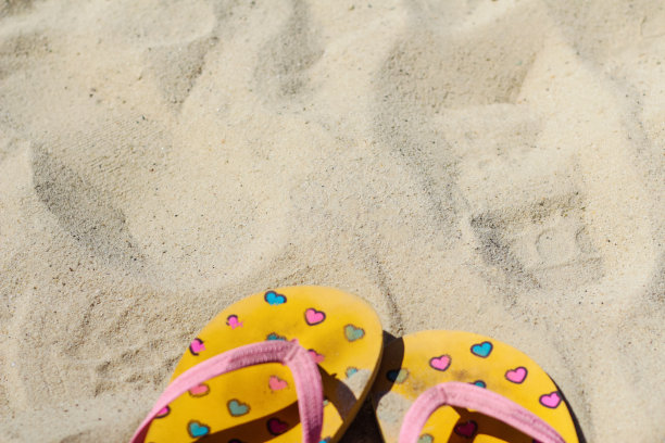 散焦亮黄色和粉色拖鞋拖鞋上有粉色和蓝色的心在沙滩上。夏天的背景。热的概念，放松和恢复，假期。的焦点图片下载