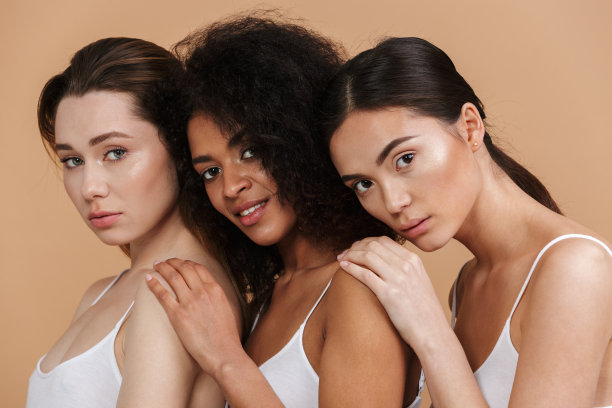 图片特写三个美丽的女人不同的国家:白人，非洲裔美国和亚洲女孩在基本的衣服，站在一起孤立的米色背景图片下载