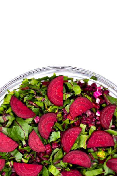 切好的新鲜叶子和甜菜根片放在一个玻璃碗里。在人造柔和的光线下拍摄的照片。图片下载