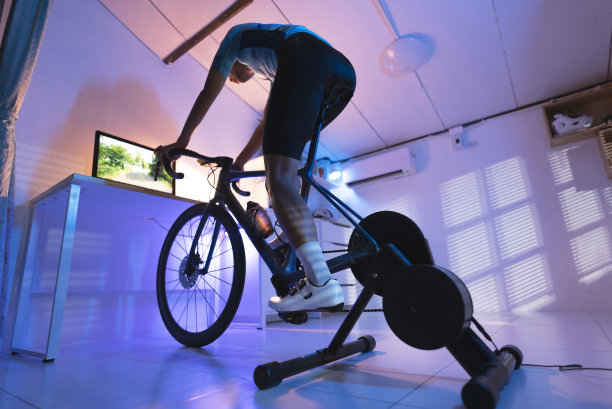 亚洲人骑自行车。她正在家里锻炼。通过骑自行车训练器和玩在线自行车游戏“t”n图片下载