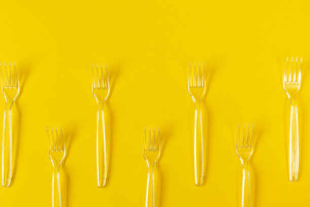 边框框架从透明的塑料叉子在黄色的背景。一次性餐具。概念餐和送餐图片下载