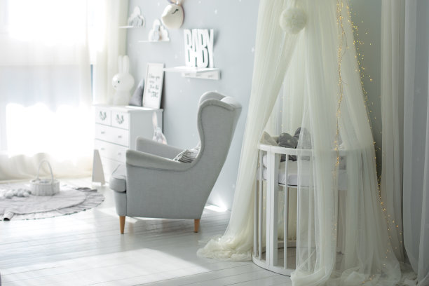 时尚的斯堪的纳维亚风格的室内新生儿室与床和灰色扶手椅。挂着白色的天篷和摇篮。用家具装饰儿童房间。现代育儿室里的婴儿床。带顶棚的婴儿床图片下载