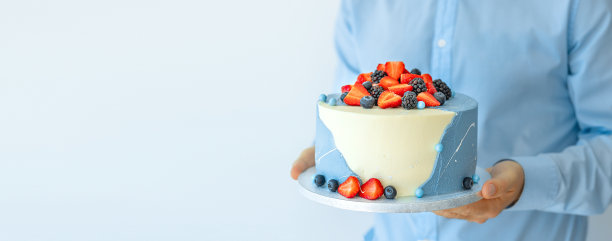 一个男人捧着一个漂亮的大蛋糕，手里拿着浆果。男厨师，厨师，糖果师或面包师。模仿太空食品的概念。横幅图片下载