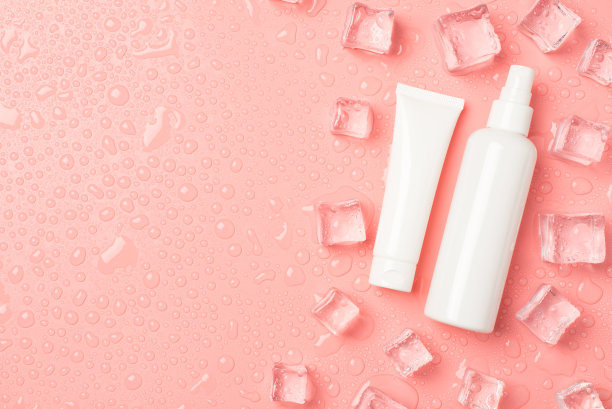 俯视图照片的白色奶油管和喷雾瓶没有标签的冰块在右边和滴在孤立的淡粉色背景与copyspace在左边图片下载