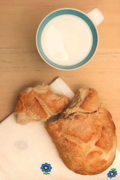 一杯牛奶和白毛巾上的新鲜面包块。木头的背景。图片下载