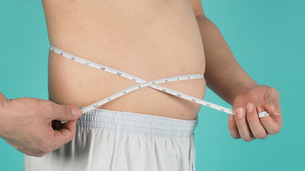 用卷尺在薄荷绿或蒂芙尼蓝的背景上测量自己的腹部。图片下载