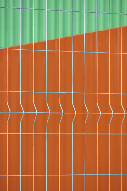 橙色钢墙和绿色金属屋顶的模糊背景的预制格栅铁丝网面板图片下载