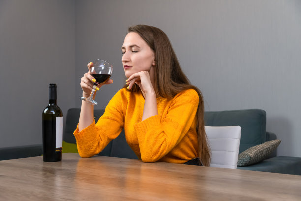 美丽的年轻黑发女子坐在客厅的一张大桌子旁，吸着一杯红酒的香气图片下载