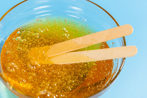 液体黄色蜡或糖膏用于脱毛和粘贴在蓝色背景。脱毛、蜜糖脱毛的概念，使皮肤光滑无毛。特写镜头。图片下载