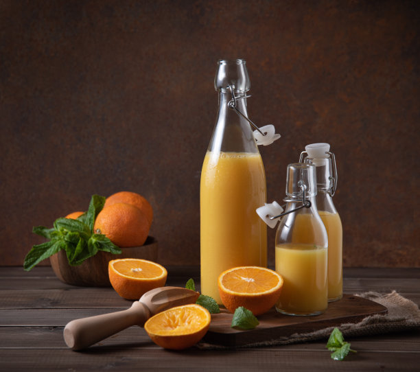 鲜榨橙汁装在三个瓶子里，切菜板上放着柑橘类水果，背景是棕色的木头。乡村的概念。前视图图片下载