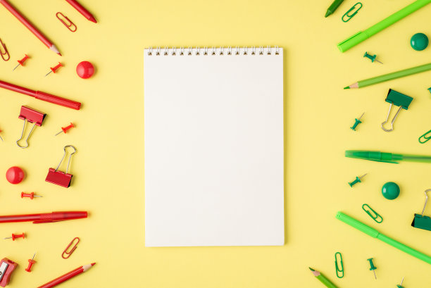 头顶照片的记事本单色绿色和红色文具铅笔、钢笔、回形针、卷笔刀和毡尖孤立在黄色的背景图片下载