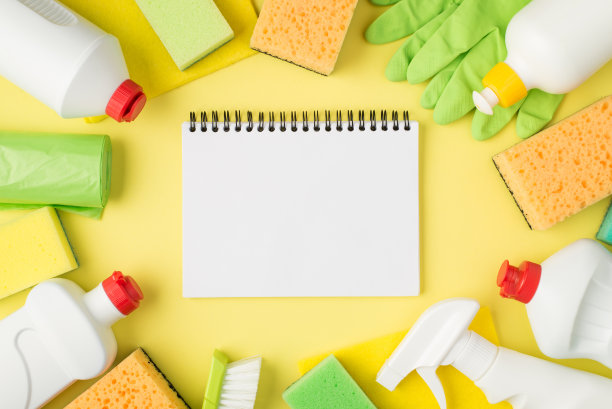 俯视图照片的计划在中间洗涤剂喷雾和凝胶瓶黄色和绿色海绵粘胶抹布垃圾袋刷子和橡胶手套在孤立的黄色背景与copyspace图片下载