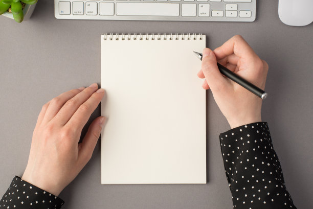 第一人称俯视图照片的女人的手握笔打开规划白色键盘鼠标花盆在孤立的灰色背景与空白空间图片下载