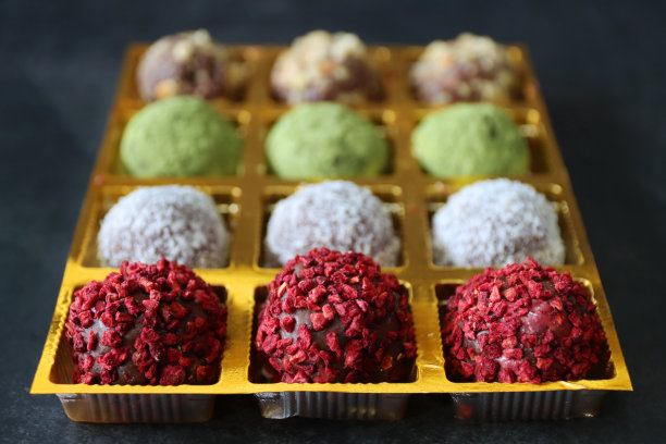 这是一组个人自制巧克力松露蛋白球的特写图片，巧克力盒里包裹着干燥的椰子、可可粉、抹茶绿茶粉和脱水覆盆子，背景是灰色的，重点放在前景图片下载