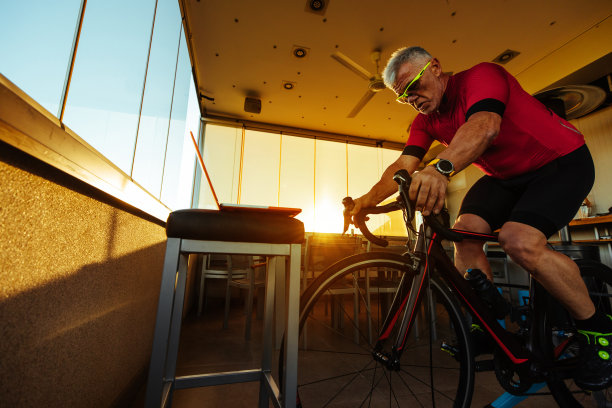 一名男子坐在健身自行车上，一边锻炼一边在笔记本电脑上看视频图片下载