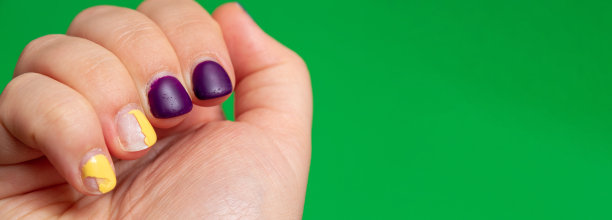 指甲上的紫色和黄色指甲油损坏。绿色背景和文字空间。有选择性的重点。图片下载