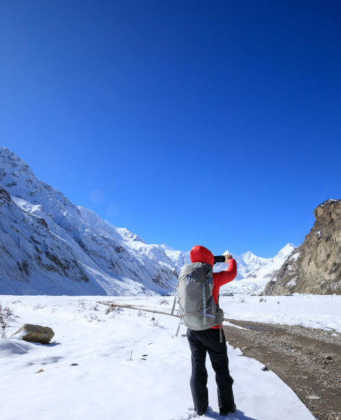 一个背包客在冬天用智能手机拍雪山照片图片下载