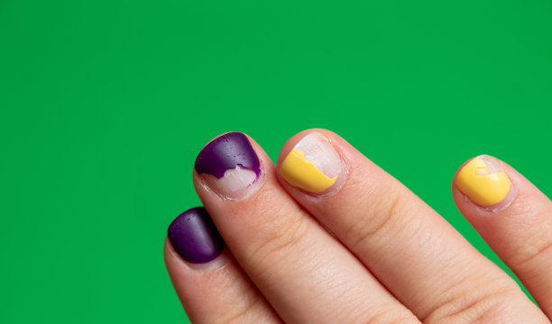 指甲上的紫色和黄色指甲油受损。绿色背景和文字空间。特写镜头。有选择性的重点。图片下载
