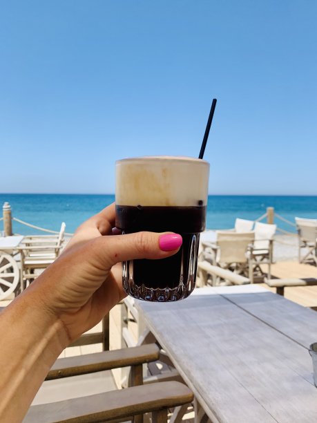 在海滩咖啡馆的女士手里拿着一杯加冰牛奶的咖啡图片下载