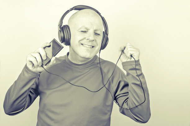 微笑的男人戴着耳机，手持数码播放器，一边听一边放松图片下载