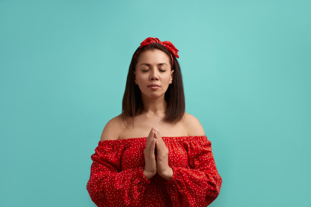 信念,希望,相信。一幅平静的女人的肖像，穿着红色的衣服，祈求着什么，保持手掌合拢，眼睛闭着，孤立在蓝色的背景下。人们表达概念。图片下载