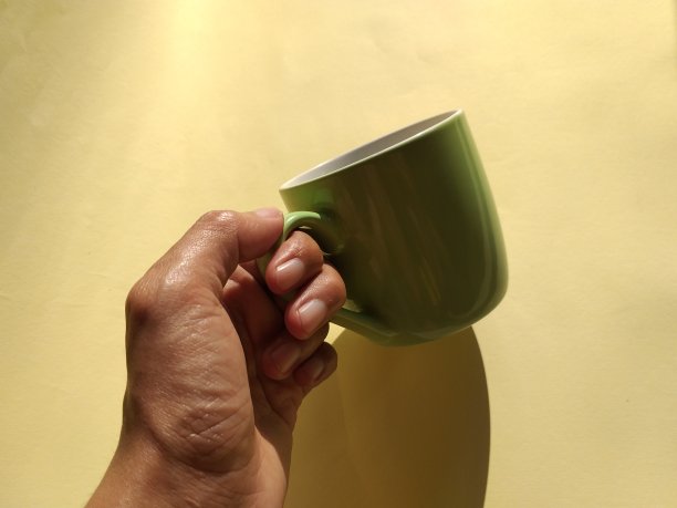 黄色背景下一只手拿着一个杯子的照片图片下载