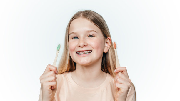 微笑的金发女孩正畸牙套拿着两个有机竹牙刷图片下载