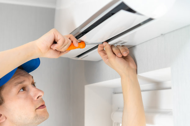 修理工穿着工装裤，手里拿着螺丝刀在修理墙上的一台空调图片下载