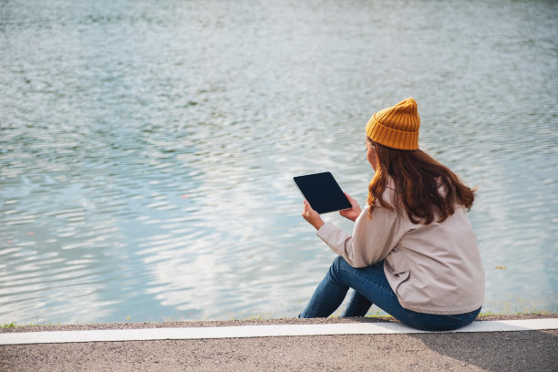 一个年轻的女人拿着并使用数字平板电脑在山和湖旅行图片下载