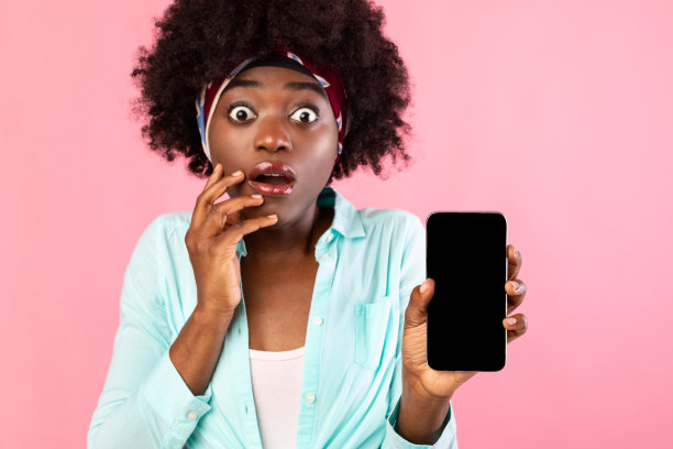 震惊的黑人妇女在粉色背景上显示智能手机黑屏图片下载