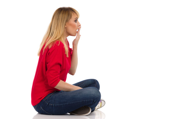 震惊的年轻女子双腿交叉坐在地板上。侧视图。图片下载