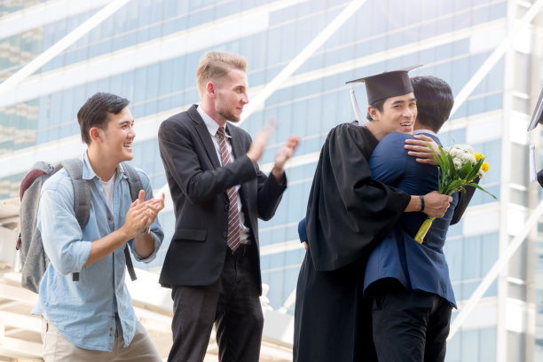 人们怀着快乐和感恩的心情，带着毕业礼服和毕业帽，与父母和朋友站在一起，在户外现代城市空间里欢快地打招呼。图片下载